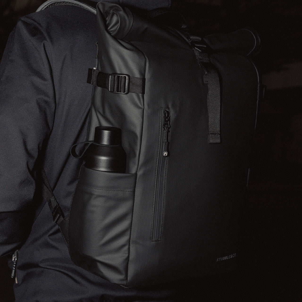 A black roll top 20l with a Stubble and Co and Ocean Bottle bottle in Black in the side pocket