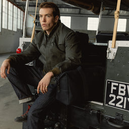 A man sitting on the back of a car with a weekender 30l in All Black next to him