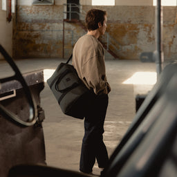 A man wearing a weekender 30l in Pirate over his shoulder and across his body using the longer strap