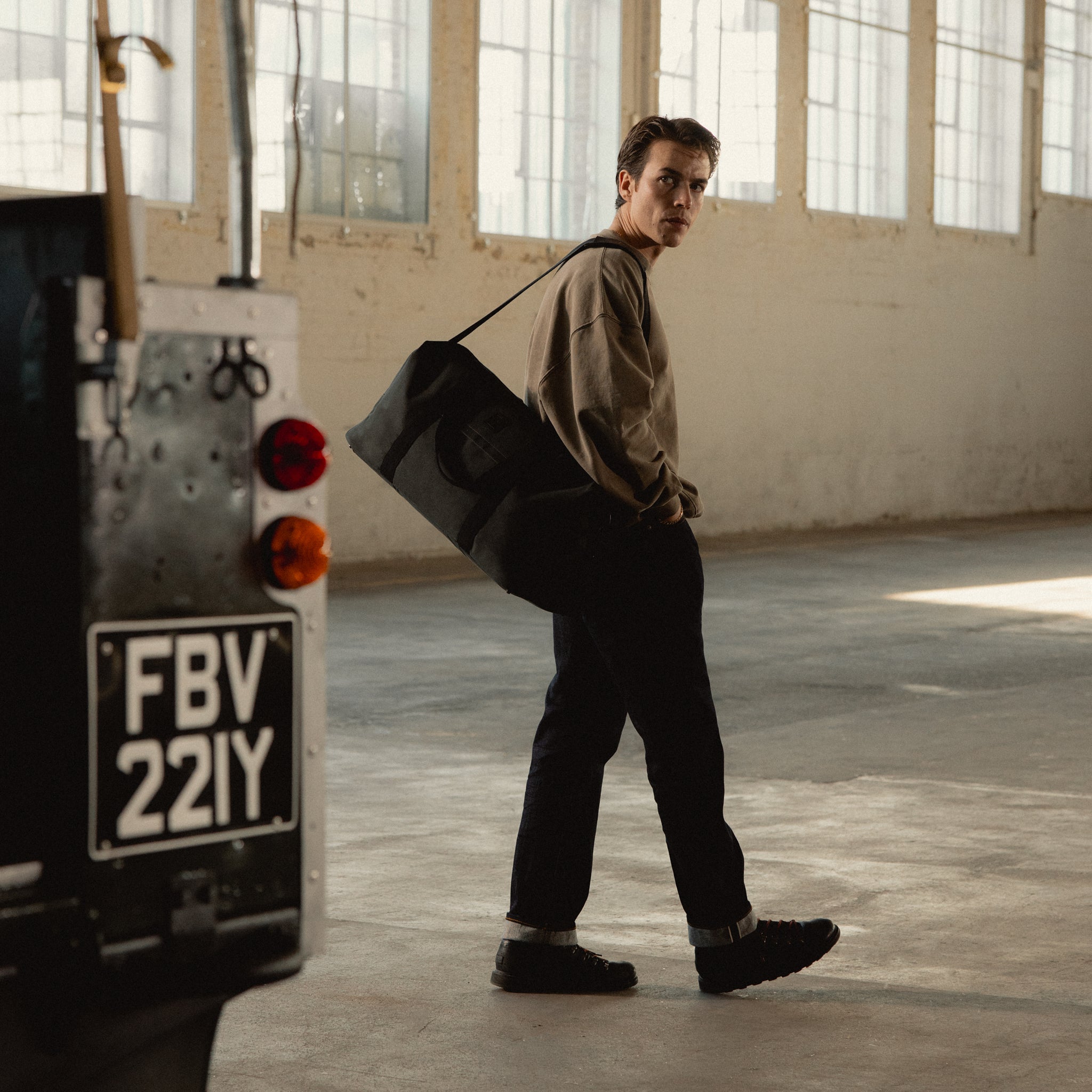 A man standing by a car wearing a Weekender 30L  in Pirate on his shoulder using the longer shoulder strap