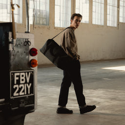 A man standing by a car wearing a Weekender 30L  in Pirate on his shoulder using the longer shoulder strap