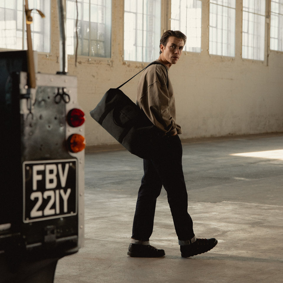 A man standing by a car wearing a Weekender 30L  in Pirate on his shoulder using the longer shoulder strap