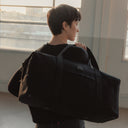 A woman facing a way holding a Weekender 30L in All Black over her shoulder