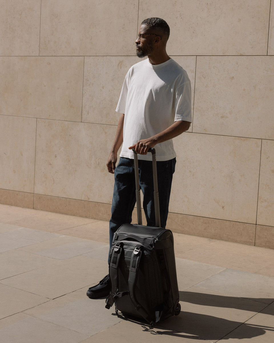A man holding the handle of the black wheeled kit bag 40l with itn ext to his side