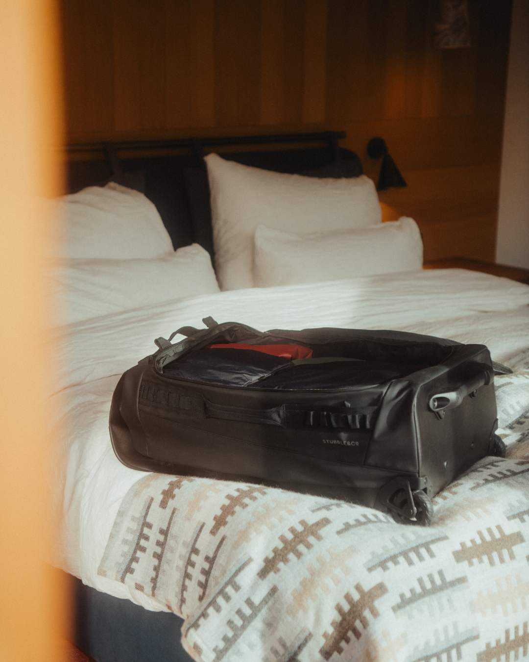 Wheeled duffel slightly open on a hotel bed.