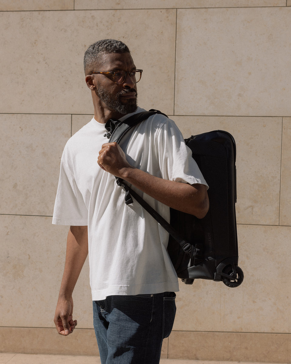 A man walking down the street wearing an All Black Wheeled Kit bag 40l on his back