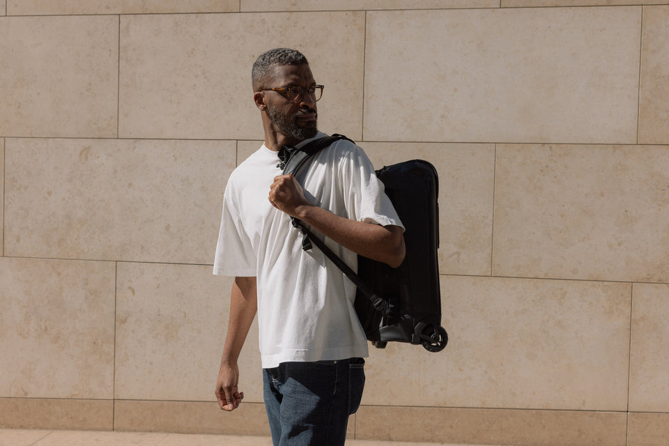 A man wearing a black wheeled kit bag 4l on his back