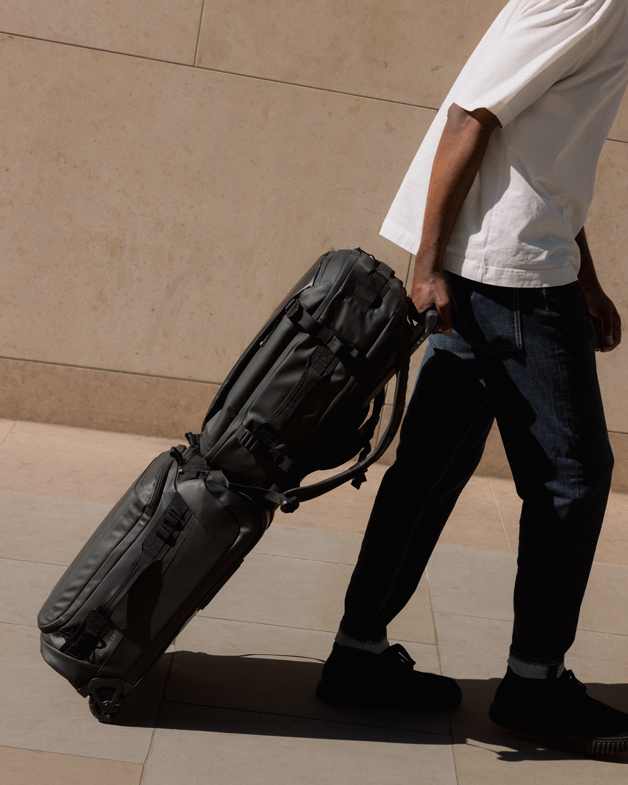 A man wheeling a Wheeled Kit Bag 40L in All Black with a Hybrid over the trolley sleeve