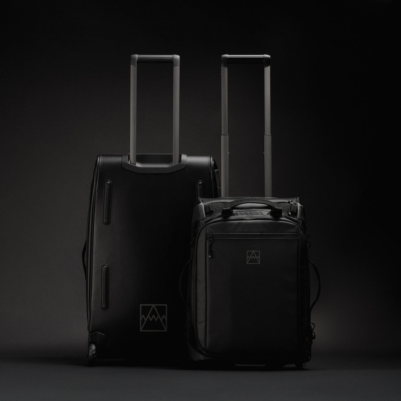 A studio shot of the Wheeled Duffel 80L and 40L side by side showing the front and back in All Black
