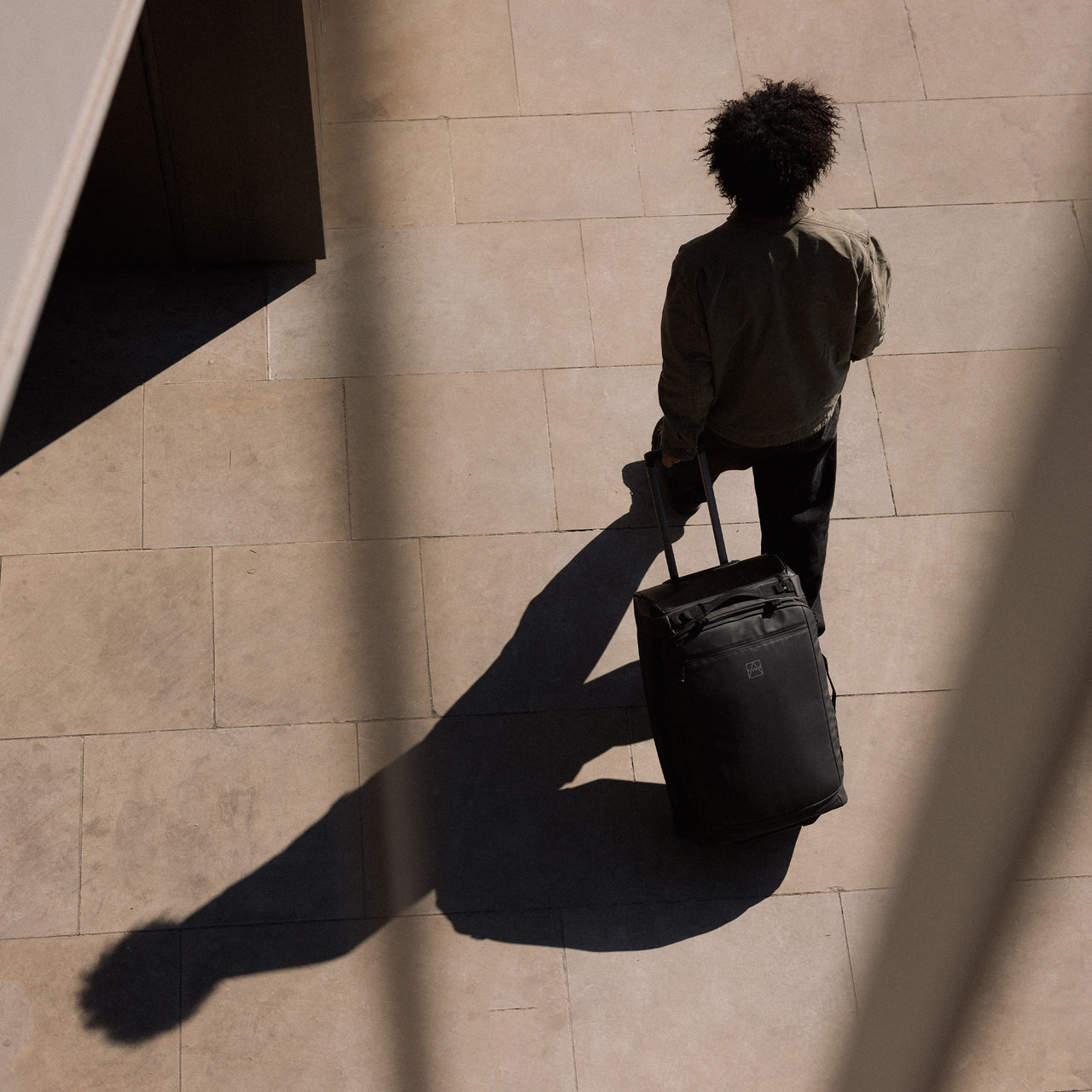 A man walking whilst wheeling a Wheeled Duffel 80L in All Black behind him