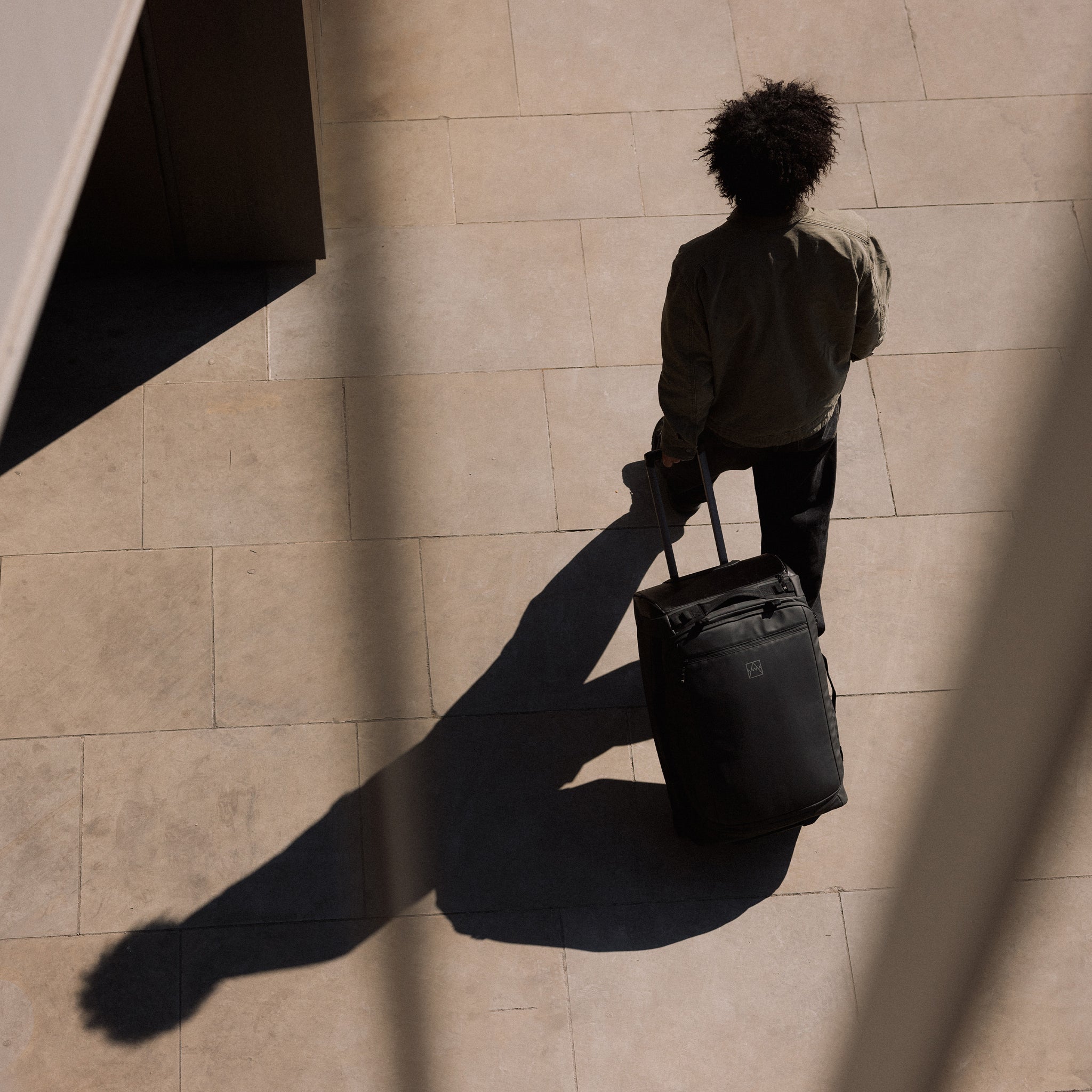 A man walking whilst wheeling a Wheeled Duffel 80L in All Black behind him