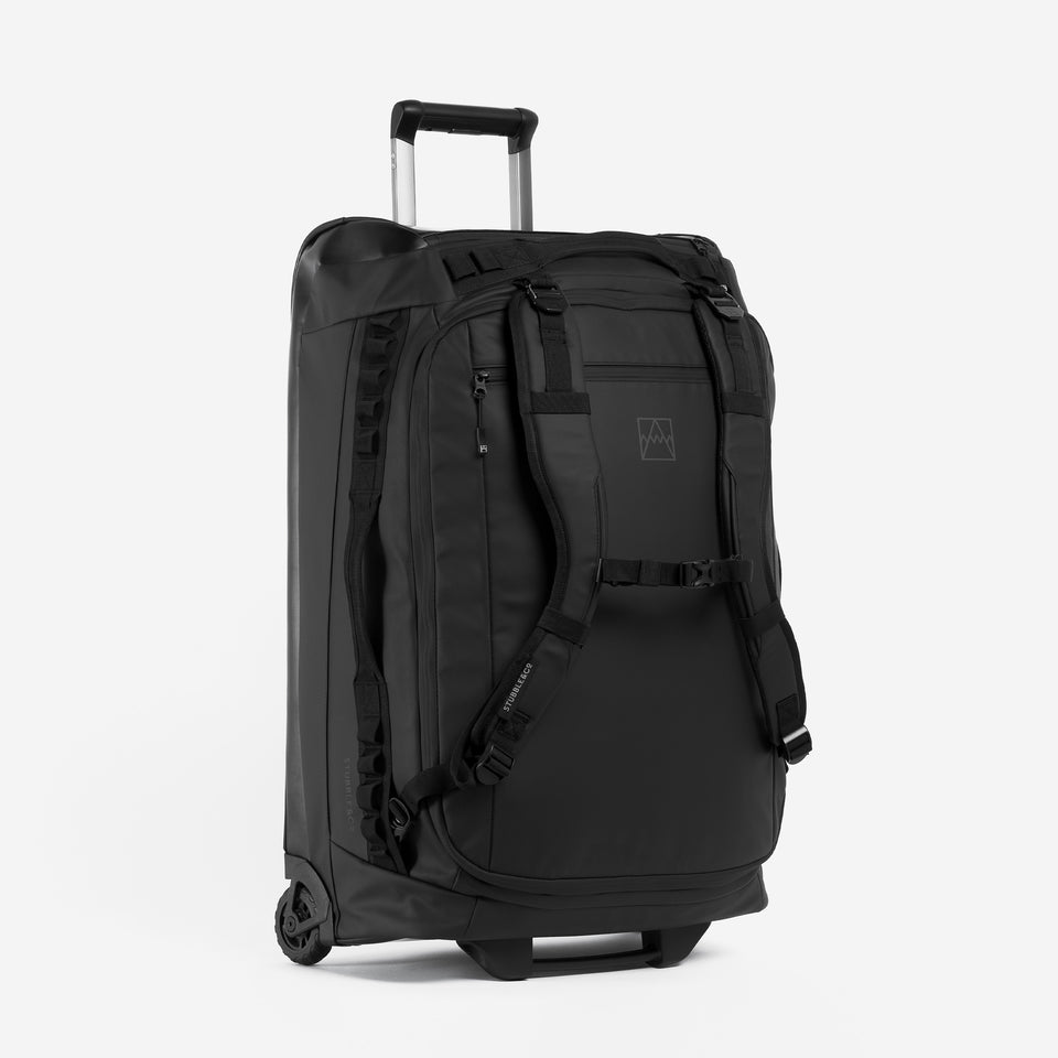 A studio shot of the All Black Wheeled Duffel 80L in All Black. It shows the backpack straps, adjustable chest strap and telescopic handle