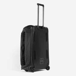 A studio shot of the All Black Wheeled Duffel 80L in All Black. it shows the back panel, reflective logo and telescopic handle