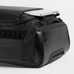 A studio shot of the All Black Wheeled Duffel 80L in All Black.  It shows the 17" Laptop Compartment