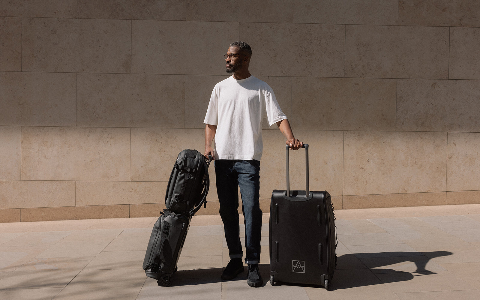 A man with luggage including the wheeled kit bag 40l and 80l in black and hybrid backpack 30l in black