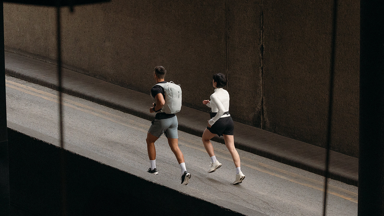 A man and woman running up a hill on the road and he is wearing the motion backpack 20l in ash