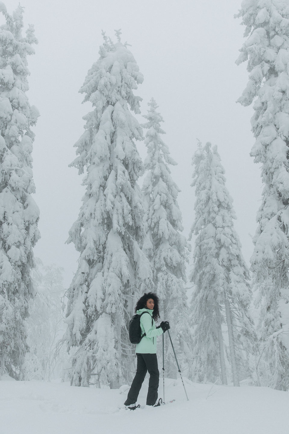 A woman standing in a snow covered forest wearing skis and a black rucksack