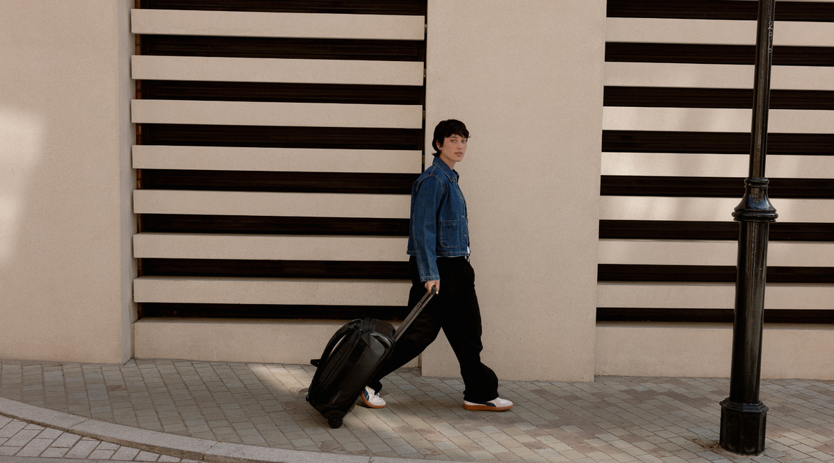 Woman walking along a pavement, pulling the Wheeled Duffel 40L in All Black.
