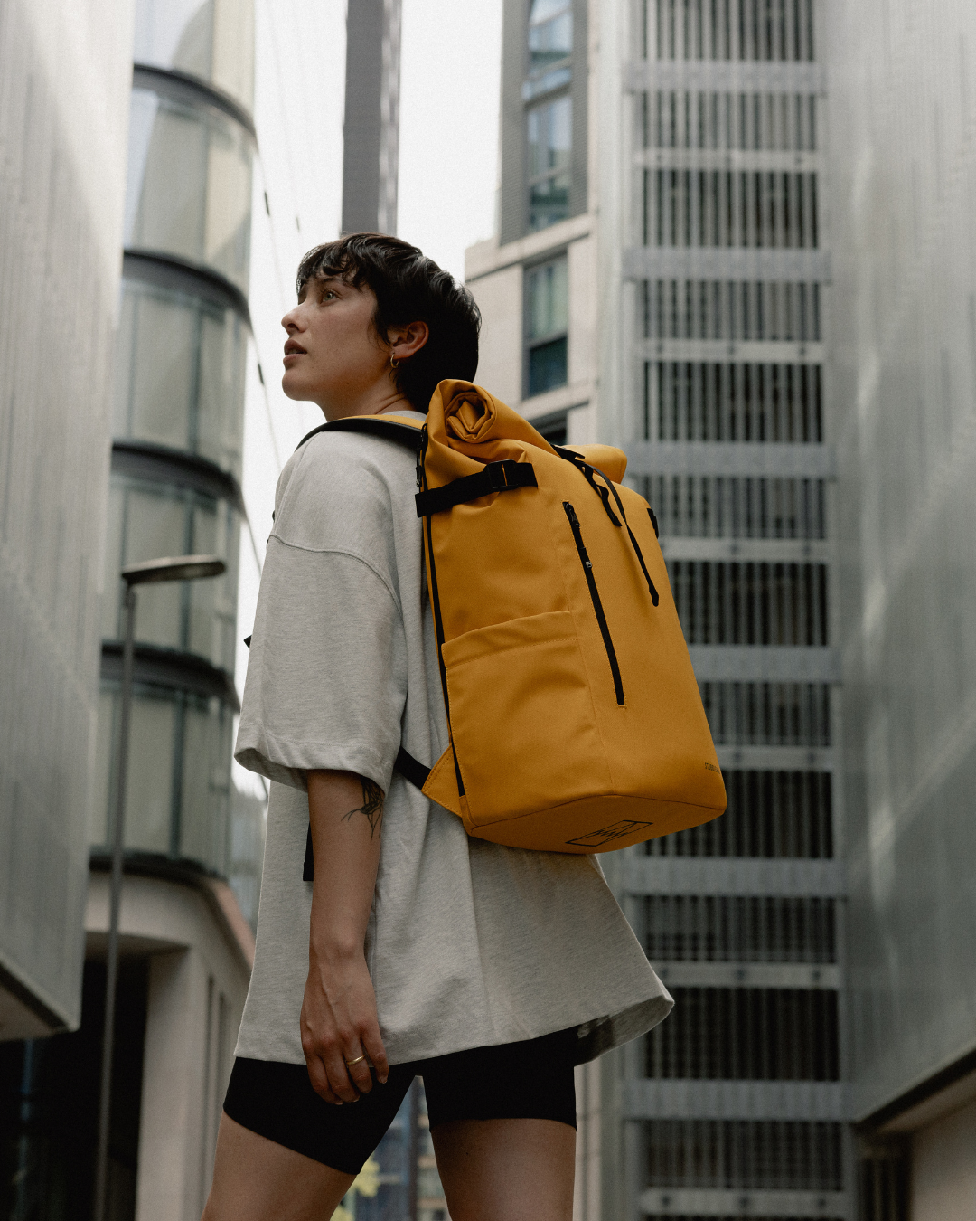 A woman walking through London wearing a Roll Top Backpack in Yellow.