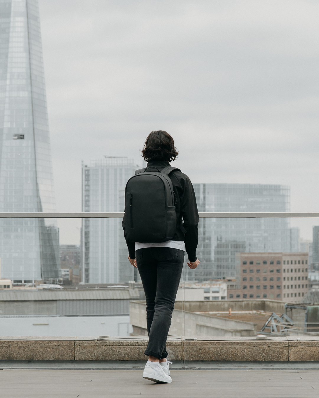 Woman wearing the Everyday Backpack in All Black, looking towards the Shard in London.