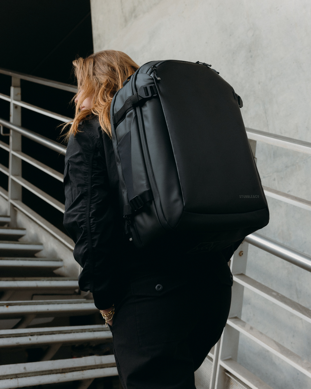 Woman walking up stairs wearing the Hybrid Backpack in All Black.