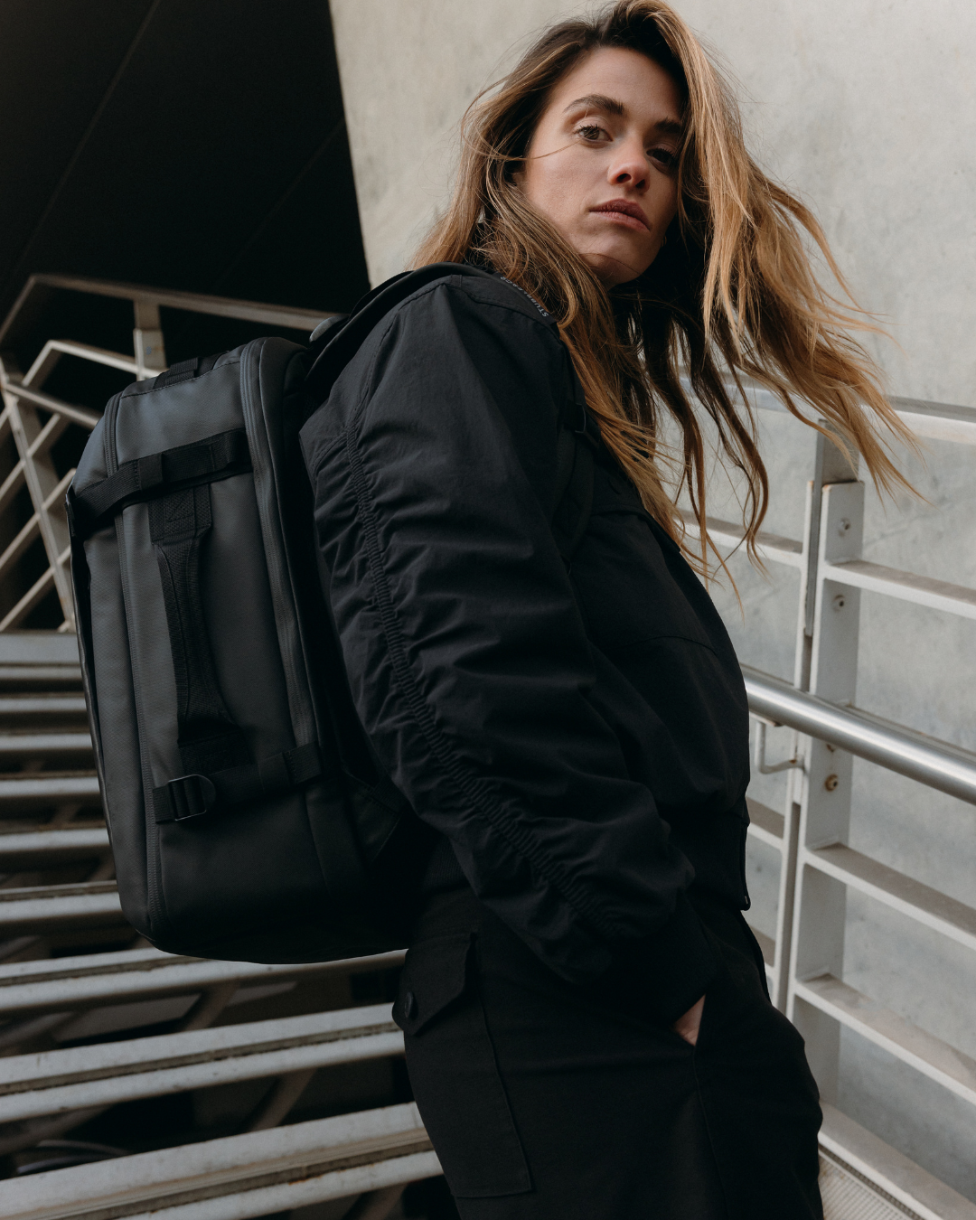 Woman in a black coat wearing the Hybrid Backpack in All Black.