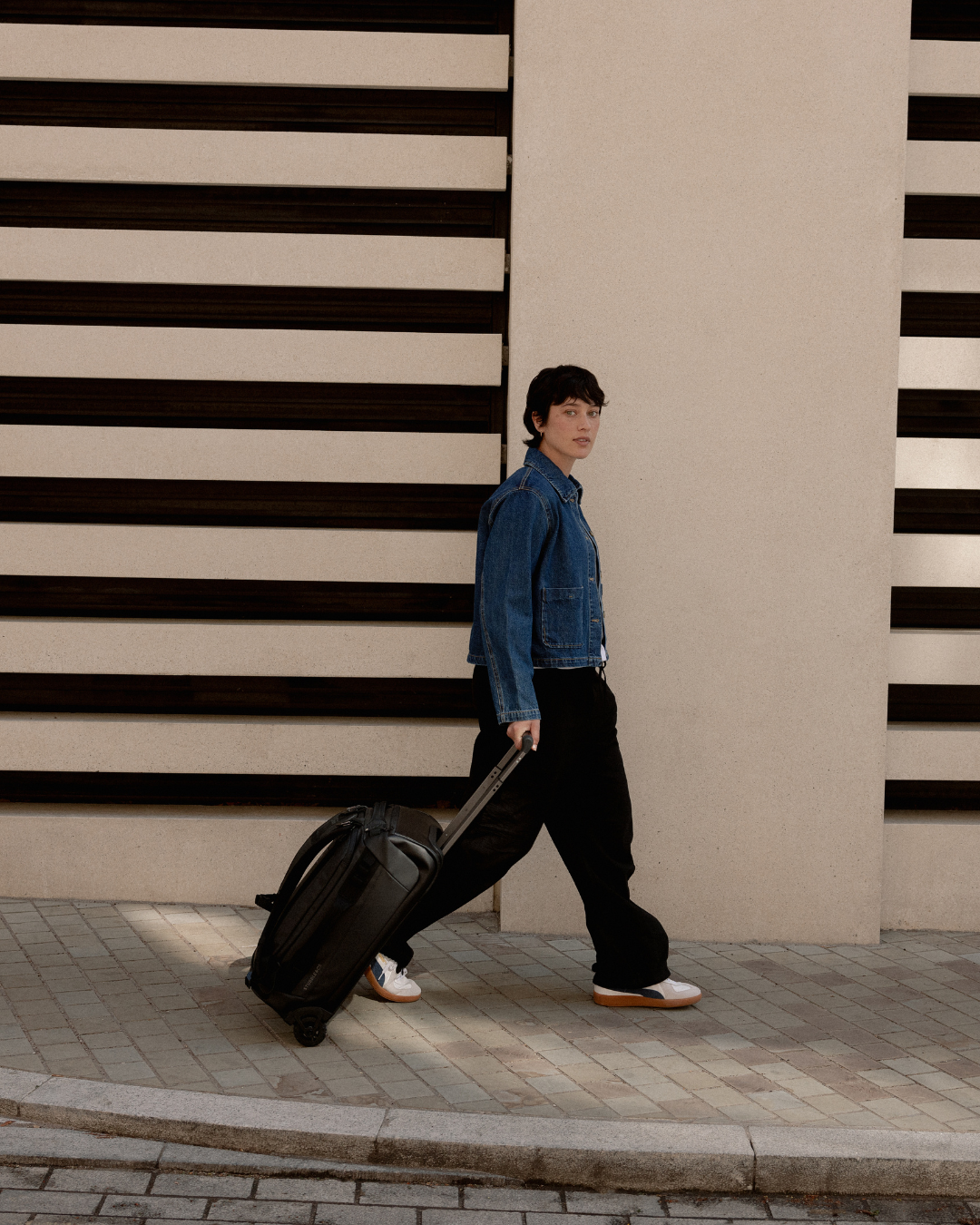 Woman wheeling the Wheeled Duffel in All Black along a London street.