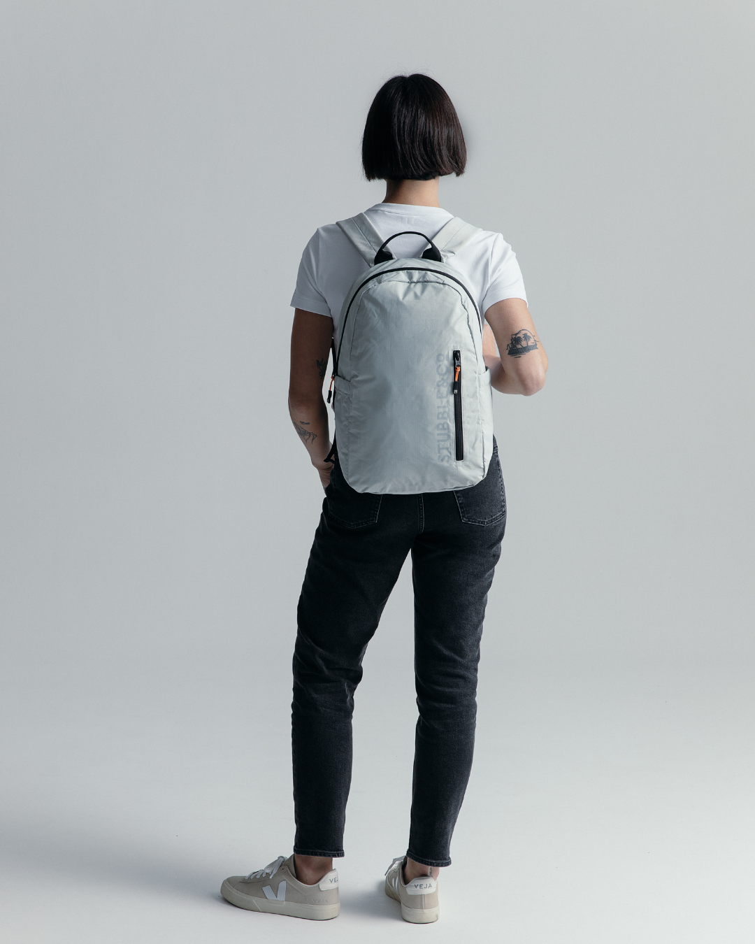 A woman wearing a white t-shirt and jeans, carrying an Off-White Packable Backpack, photographed from behind.