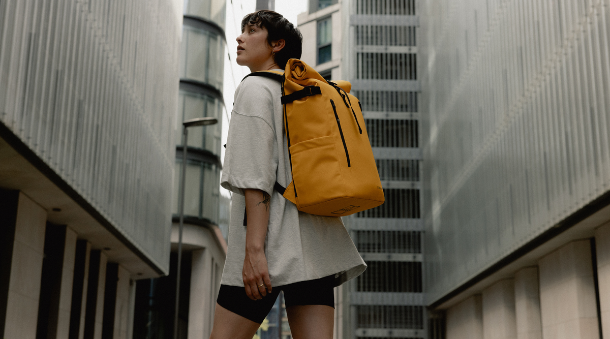 A woman wearing a Roll Top Backpack in Yellow, walking through a London street.
