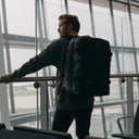 Back view of a man wearing The Adventure Bag in All Black while standing in an airport.