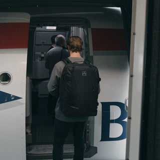 Back view of a man boarding a plane wearing The Adventure Bag in All Black.