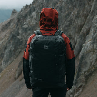 The Adventure Bag in All Black being worn by a man. Shot from the back while stoof in the rain.