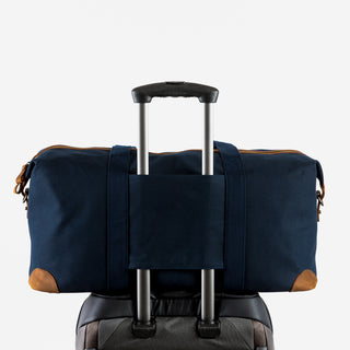 Studio shot of The Weekender in Navy with the trolley sleeve over a suitcase handle.