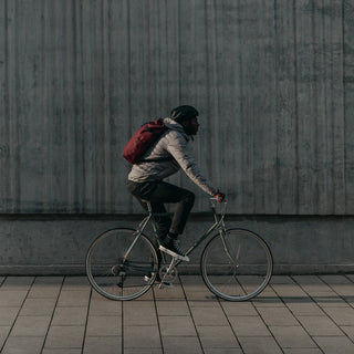 Side view of a man riding a bike in a grey coat wearing The Roll Top in Earth Red