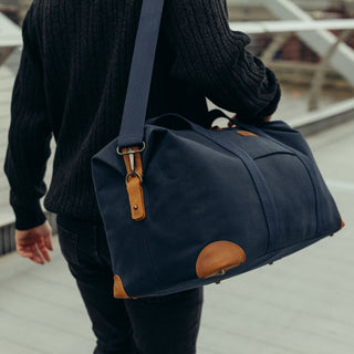 A man walking away from the camera with The Weekender in Navy over his shoulder.