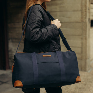Side view of a woman walking past the camera with The Weekender in Navy over her shoulder.