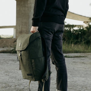 A man holding The Backpack in Olive by the top handle.