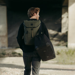 A man walking away from the camera with a backpack on his back and The Weekender in All Black over his shoulder.