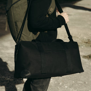 A man with The Weekender in All Black over his shoulder and a backpack on their back.