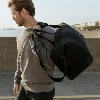 Side view of a man walking past the camera with The Weekender in All Black over their shoulder.