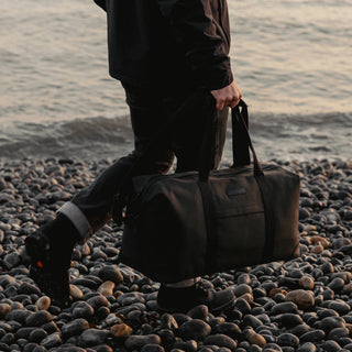 A man walking on a beach holding The Weekender in Pirate by his side.
