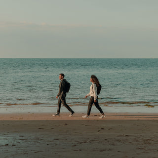 Side shot from afar of a man and women walking by the sea with The Backpack Mini on.