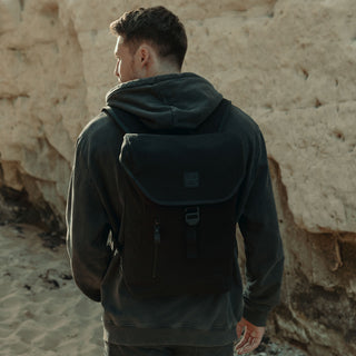 Man in a grey hoodie wearing The Backpack Mini in All Black, shot from the back.