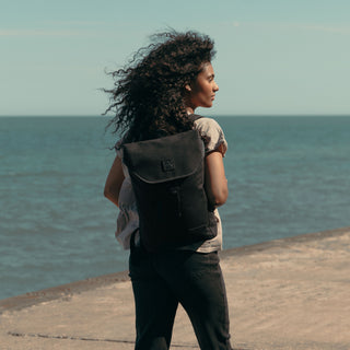 A women stood with her back to the camera, looking to her right as she wears The Backpack Mini in All Black.