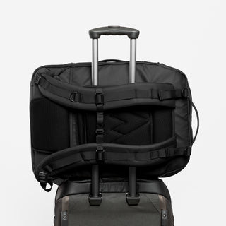 The Adventure Bag on it's side, in All Black shot from the back, with the Trolley Sleeve being used on a suitcase.